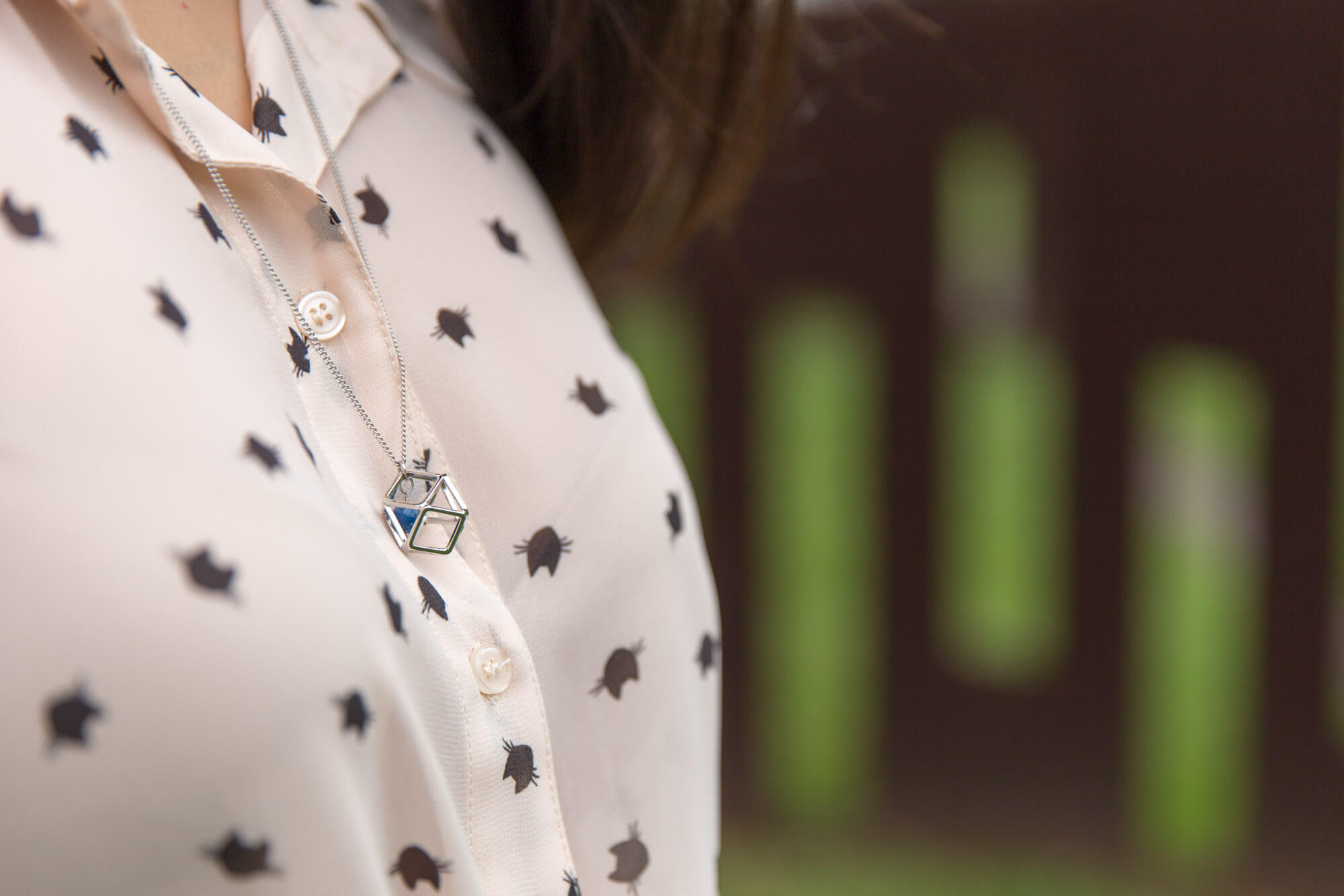 A closeup of a woman’s necklace resting on her sternum, seen from the side. She is wearing a light coloured shirt