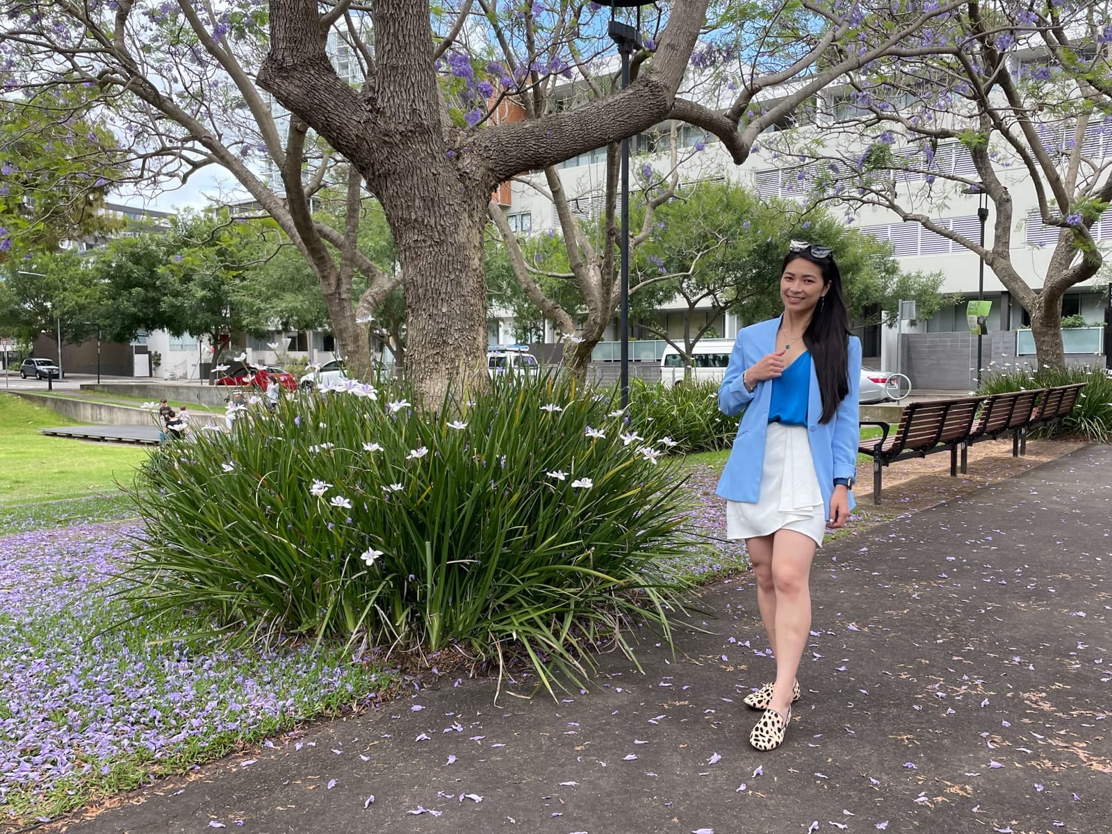 The same woman in previous photos in this post, wearing the same outfit and in the same location. She has sunglasses on top of her head and is standing with one leg slightly in front of the other.