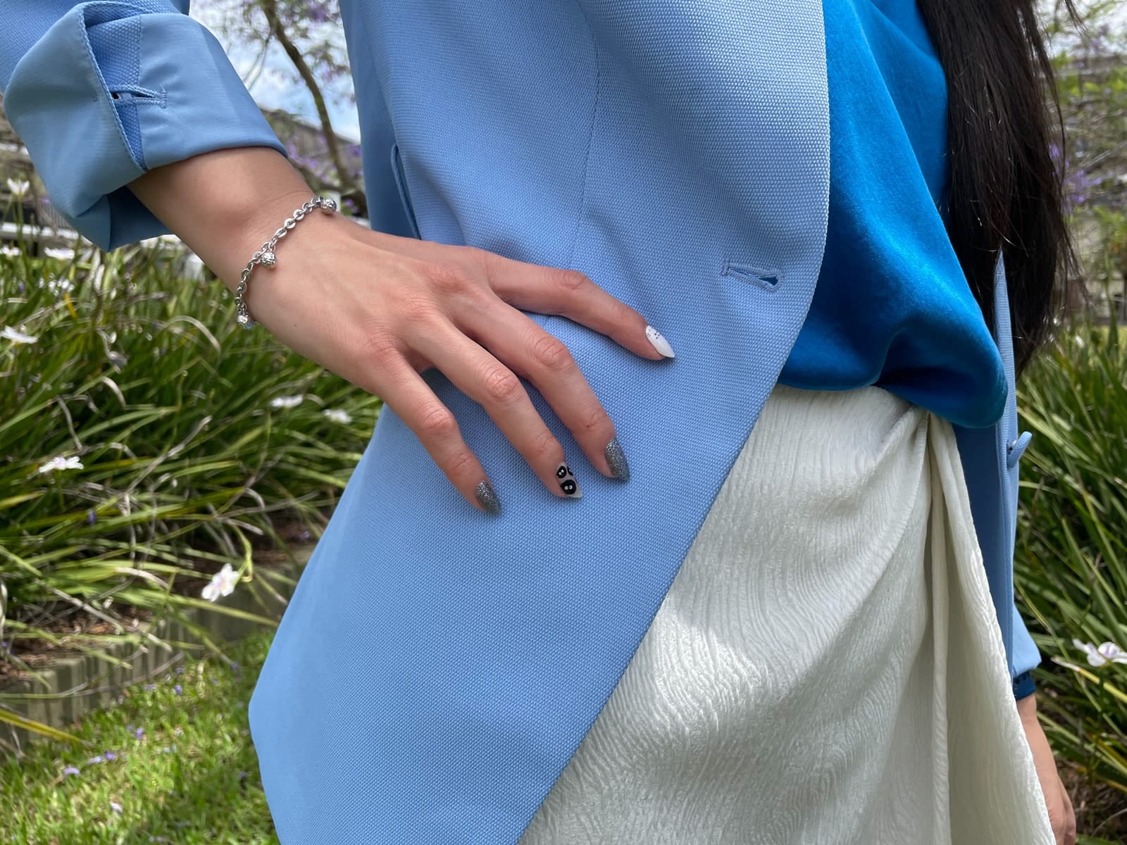 A close-up of a woman’s hand on her hip. She is wearing a blue blazer and a white skirt. Her nails have nail art of Totoro