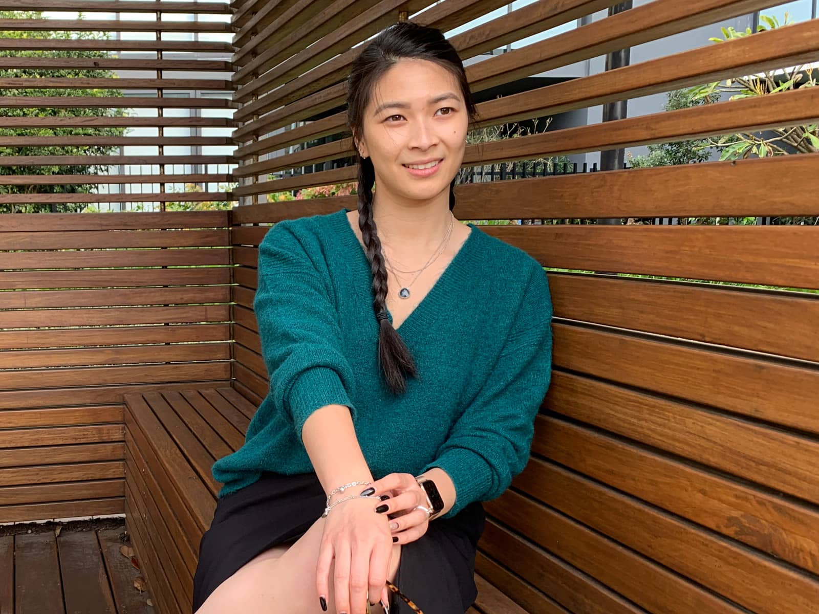 A medium shot of the same woman in other photos on this page; she is looking into the distance and has her hands placed delicately on one knee, which is crossed over the other. She is sitting in a wooden cabana