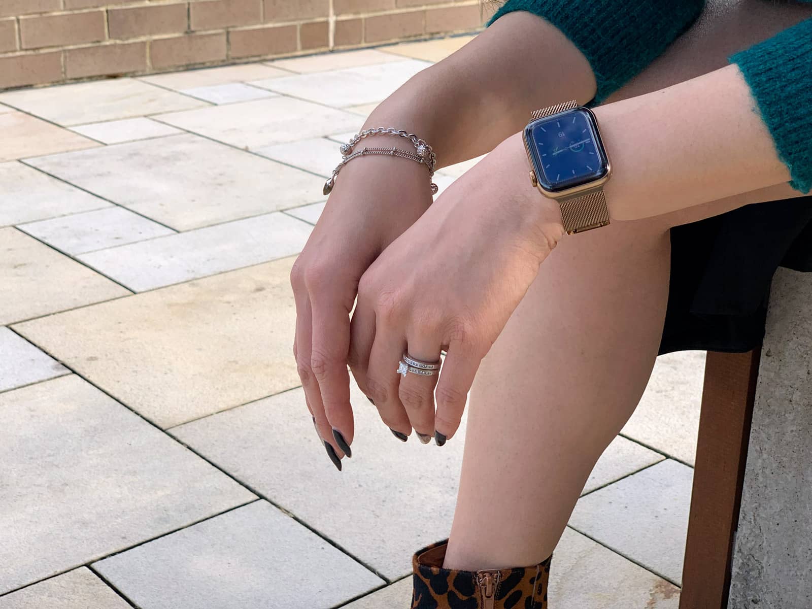 A close-up of a woman’s hands. She is wearing a gold watch with a digital face, a wedding and engagement ring, and a couple of bracelets.