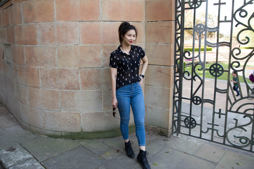 Me posing with one leg slightly in front of the other near a brick wall and a decorative gate