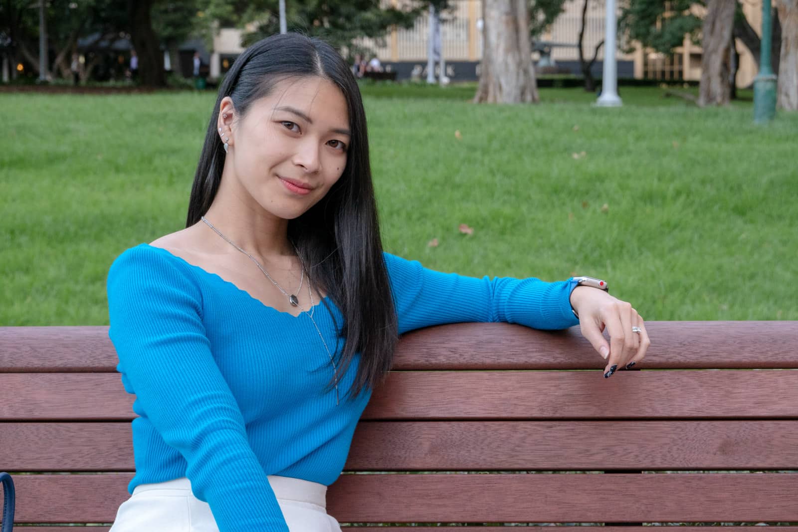 The same woman in other photos on this page, sitting on a wooden bench, with an arm over the back of the bench. She is looking at the camera and smiling.