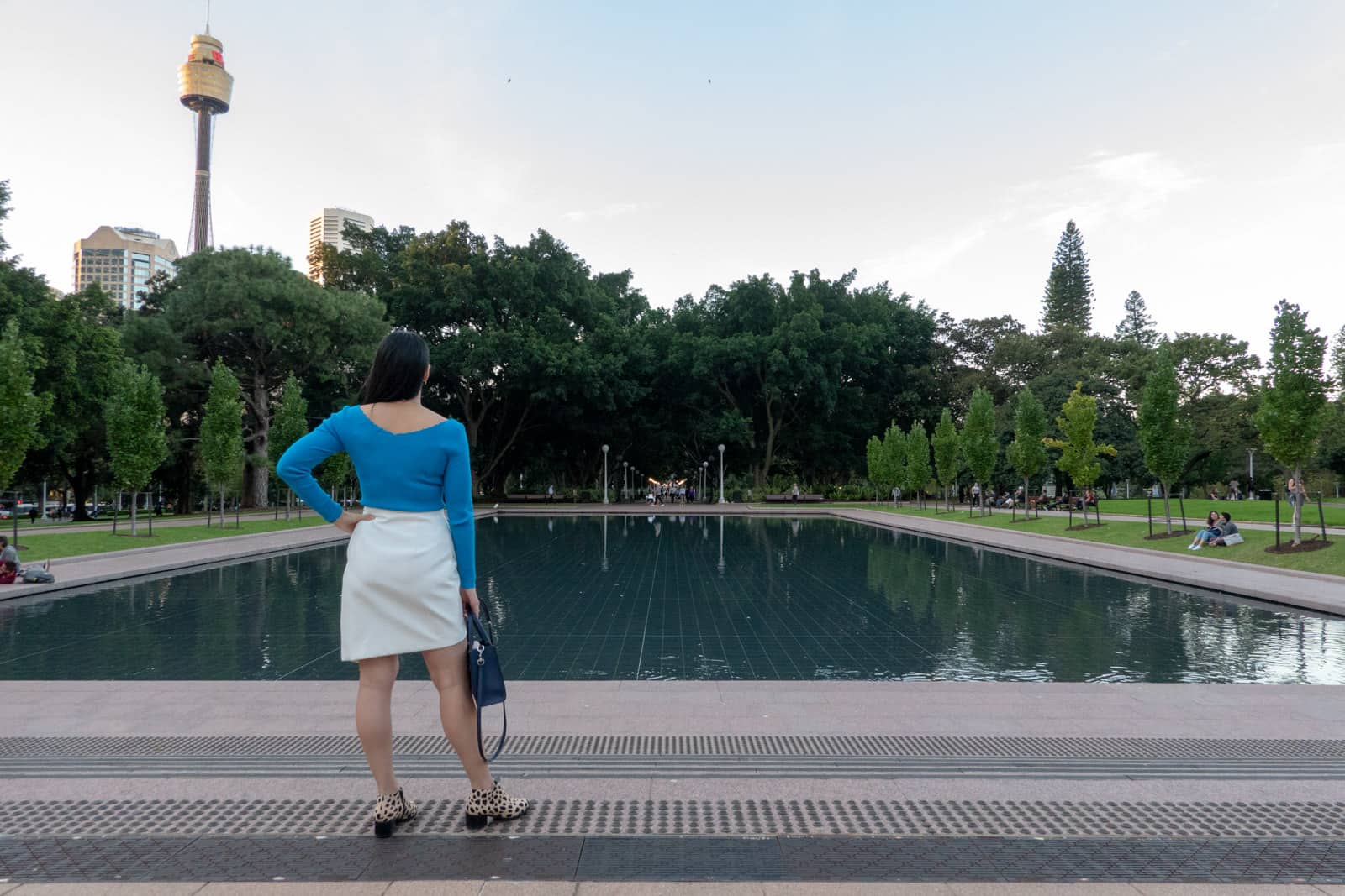 The same view as the previous picture, with the woman facing away from the camera. She has a hand on her hip and there are also less passersby standing in the vicinity.