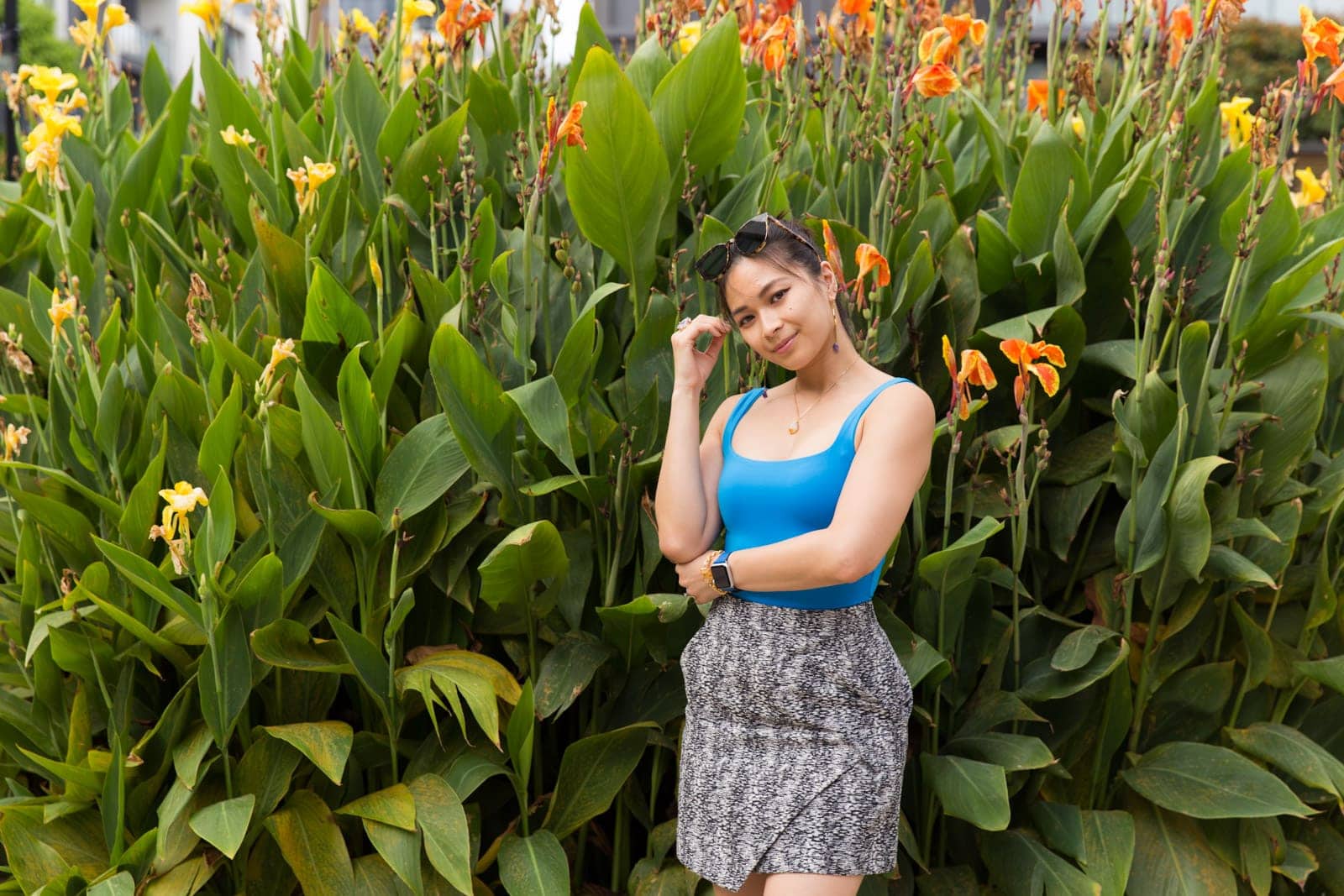 A medium shot of the same woman in other photos in this post, in the same outfit. She has a hand near her face, with that arm propped up by her other arm horizontally across her body