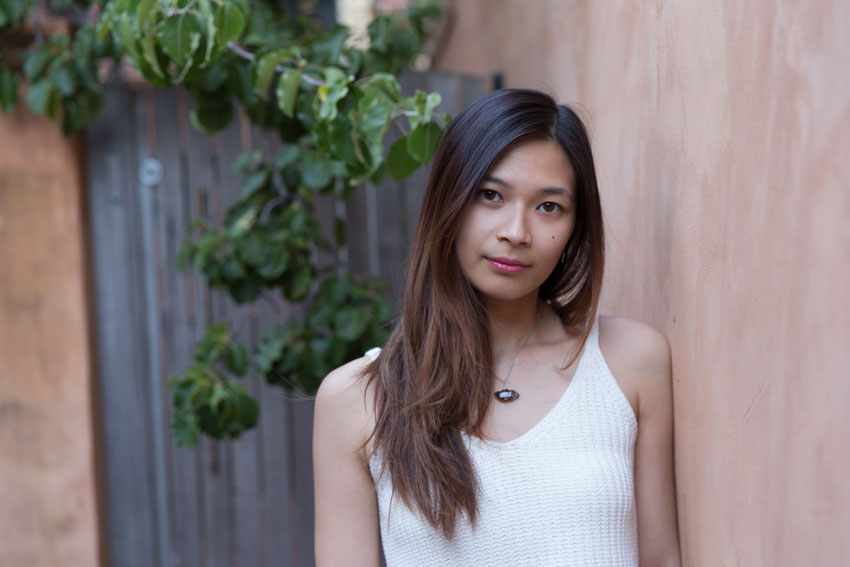 Close shot of me leaning against a brown-red wall with a wooden gate in the background