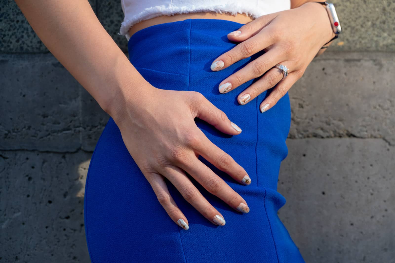 Close shot of a woman’s hands at the side of her hip. She has pastel nail art on her fingernails and is wearing a figure hugging blue skirt
