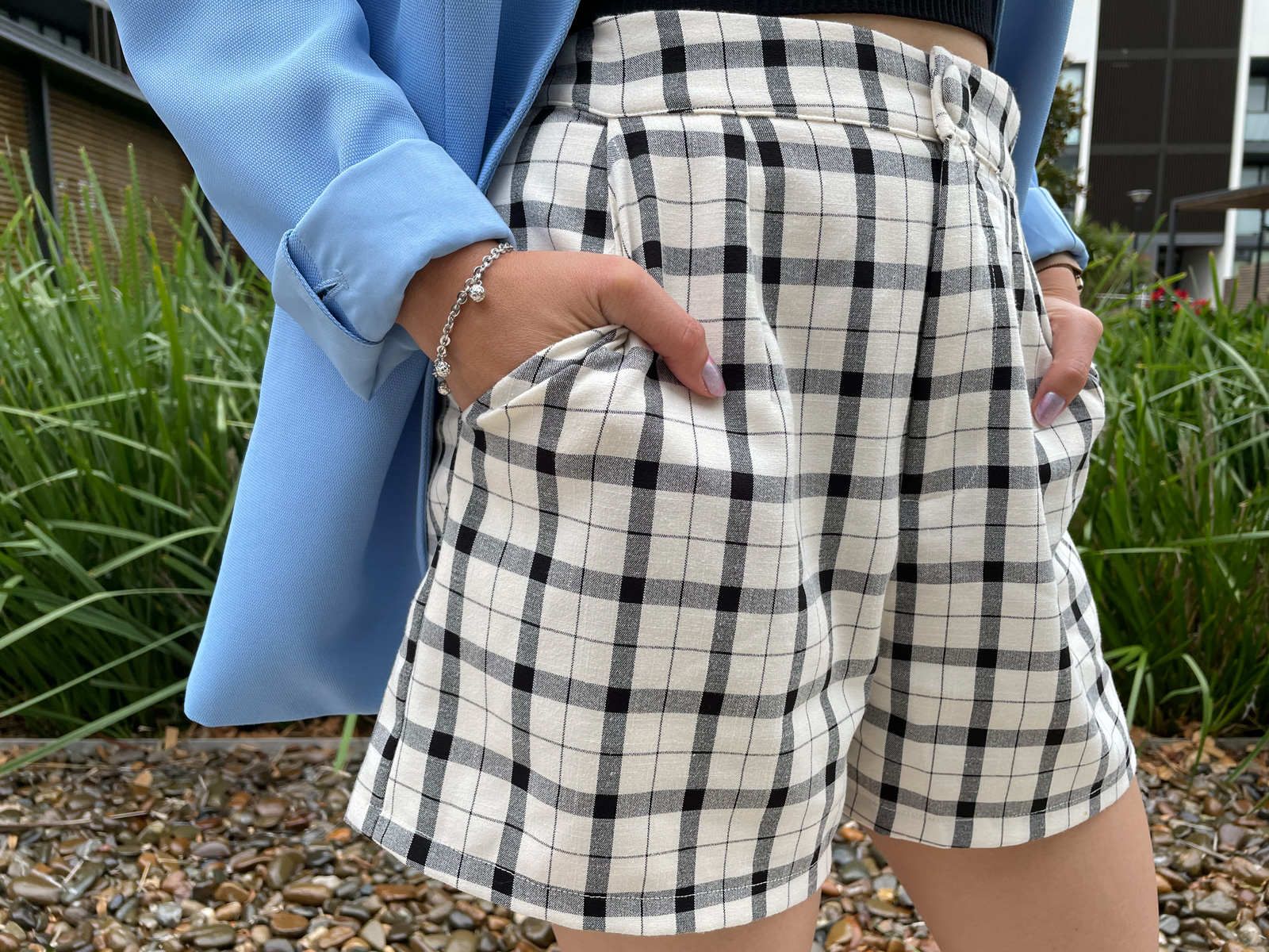 A close-up of a woman wearing shorts with a plaid print. She has her hands in the pockets.