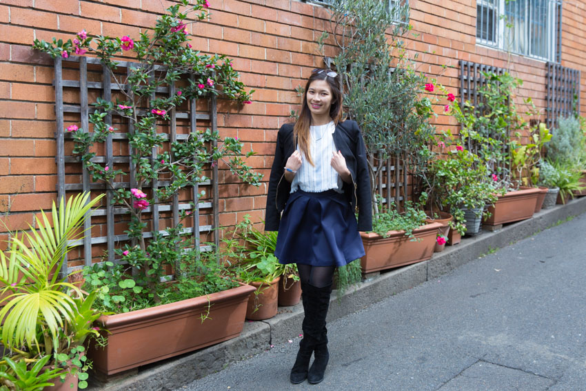 Me with my jacket on my shoulders in front of an old building with flowers and plants down the side