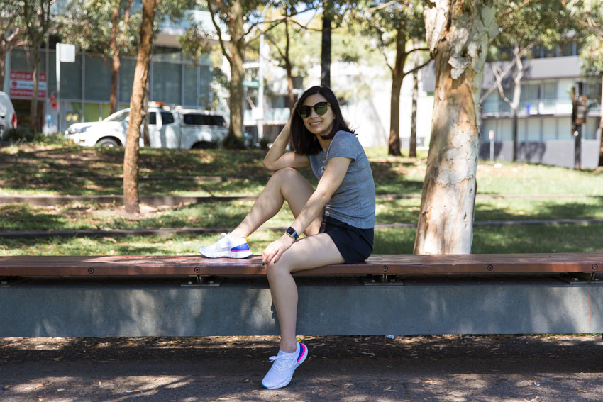 Me sitting on a bench with my left leg hanging down and just touching the ground, my right leg balanced with my foot on top of the bench. My right elbow is resting on my right knee and I am facing the camera with my sunglasses over my eyes.