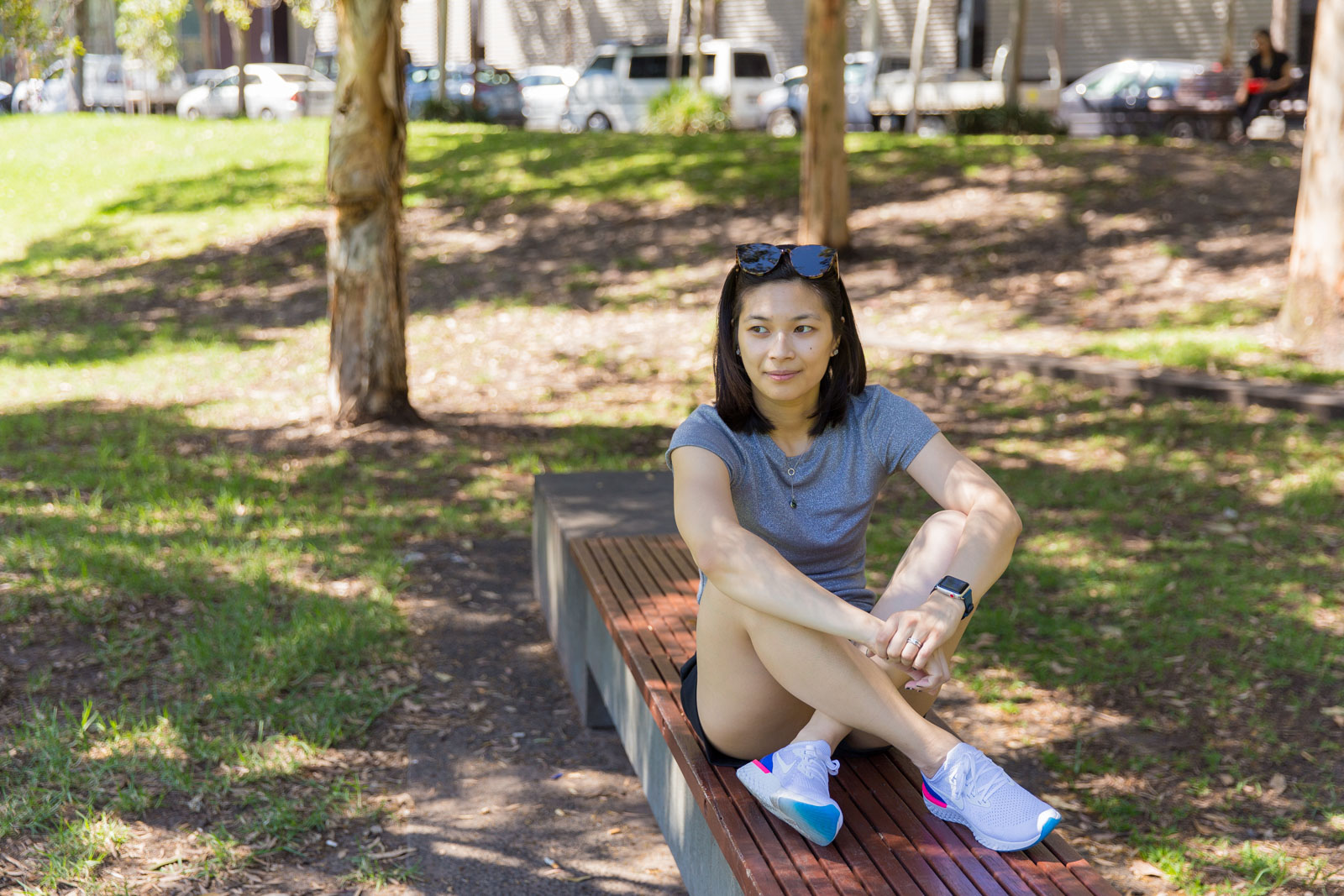 Me sitting on a flat concrete bench with a wooden top. My knees are raised with my ankles crossed in front, and my elbows rest on my knees as I gaze somewhere away from the camera.