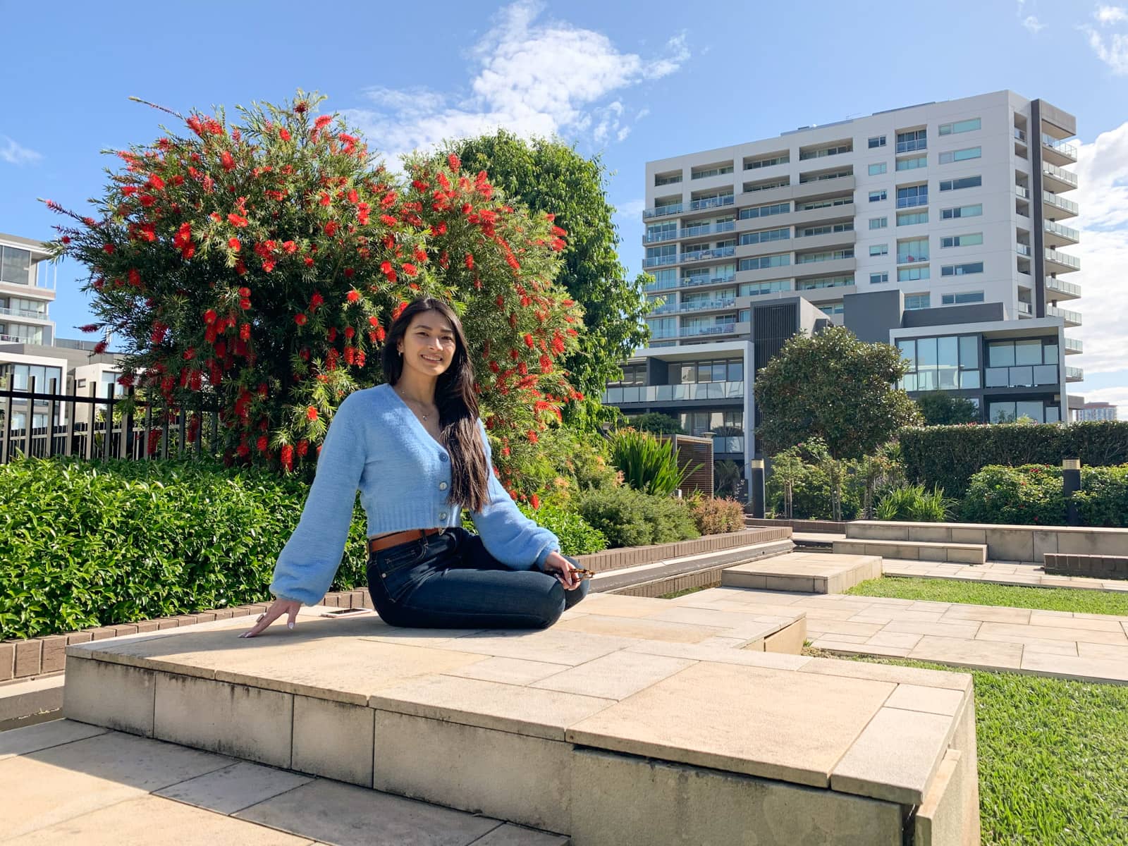 The same woman in the other photos on this page, in the same outfit. She is sitting on a stone step and has a hand out to the side for balance. Both her legs are tucked away to one side.