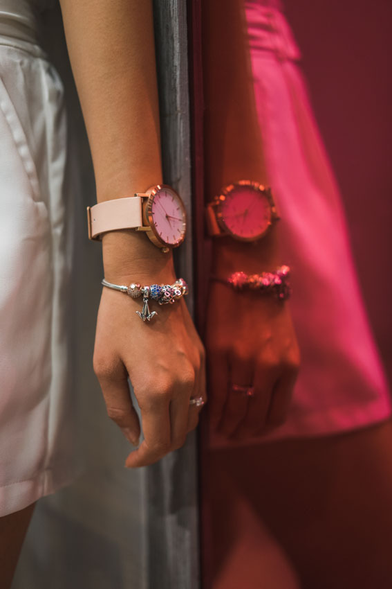 Close shot of my wrist with a Pandora bracelet and round-faced watch, against a red tinted mirror