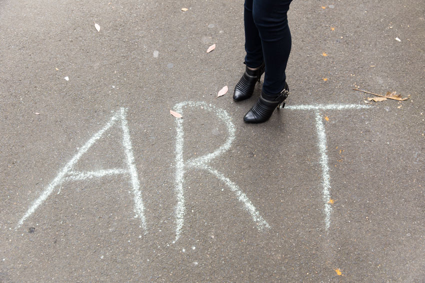 My shoes as I stand near a chalked piece of writing reading “ART”