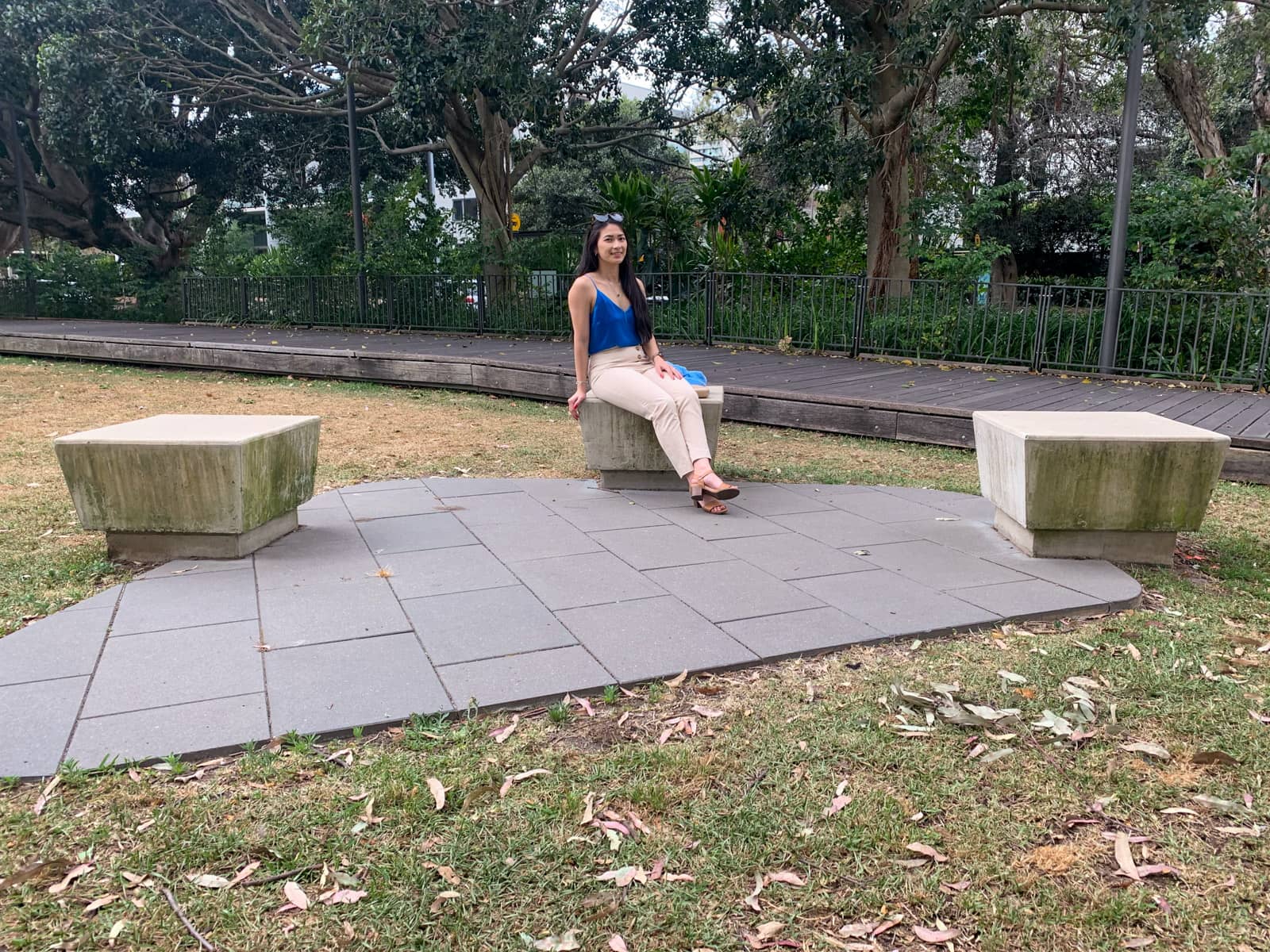 The same woman in the previous photos on this page, in the same outfit. She is sitting on a concrete slab about the same height as a chair. Two other similar slabs are nearby.