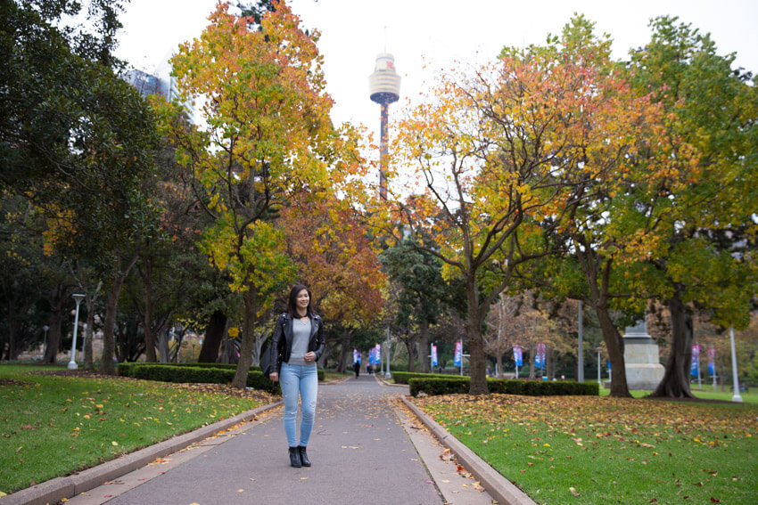 The same woman in the previous photo, wearing the same outfit and in the same setting. It’s a landscape view with some high-rise buildings visible behind the trees