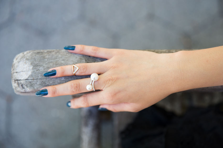 My hand with dark teal painted fingernails, wearing a pearl ring and a gold midi ring