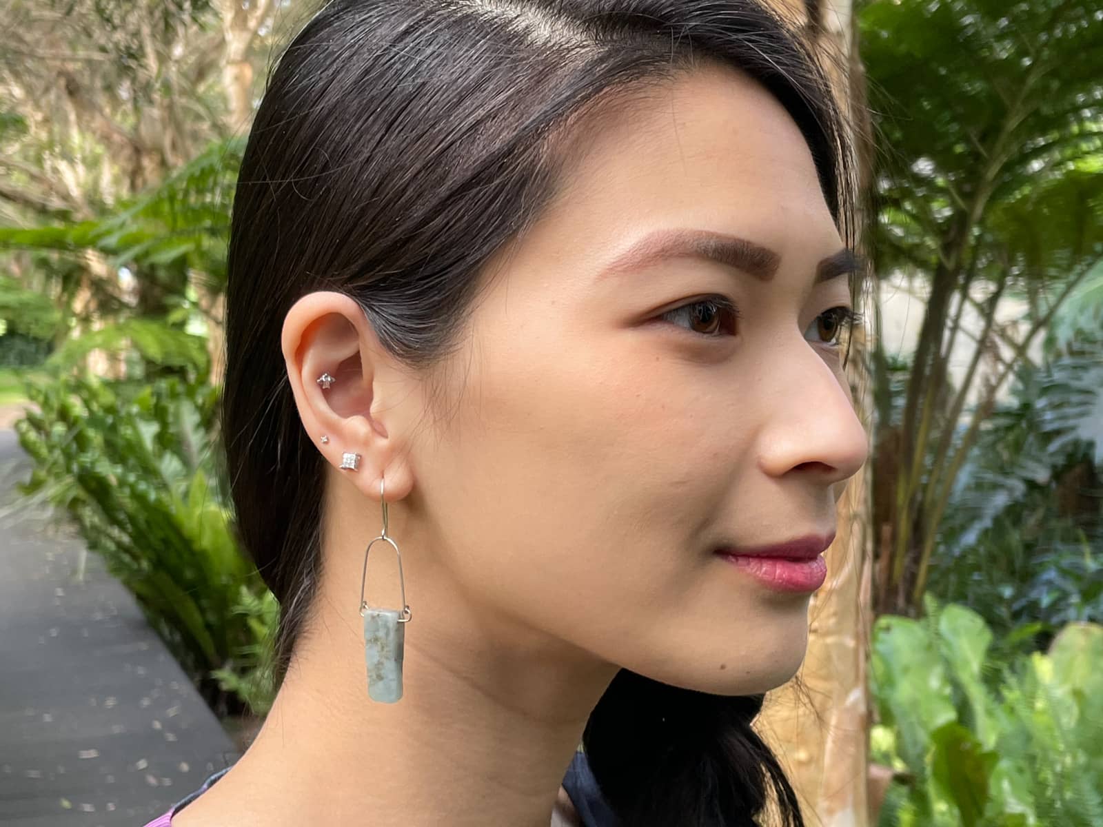 A close-up of a woman’s face from the side. She has silver earrings in her ear, with the bottommost earring being a silver wire earring with a raw aquamarine stone drop