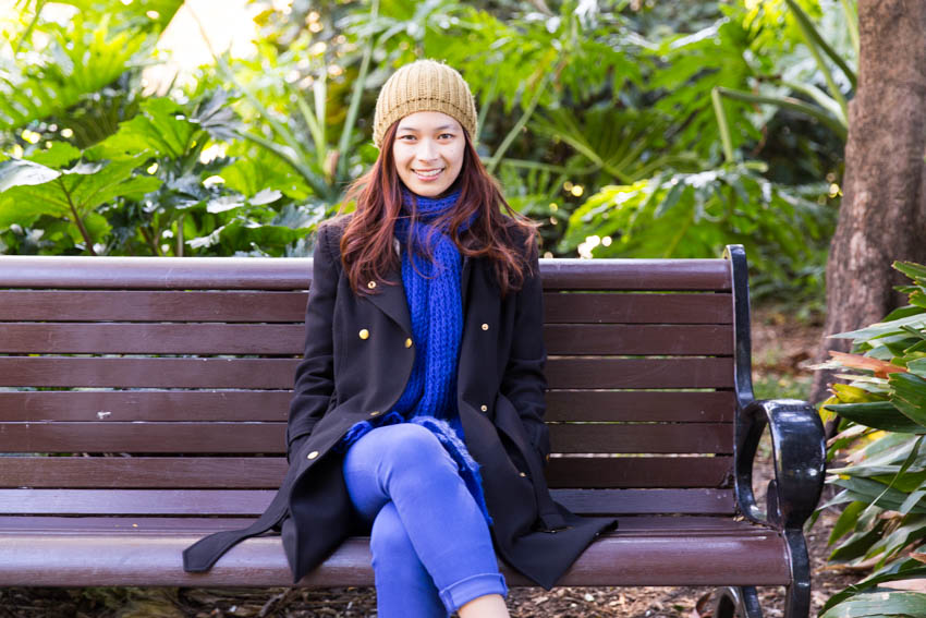 Me sitting on a wooden bench in my coat, beanie and scarf