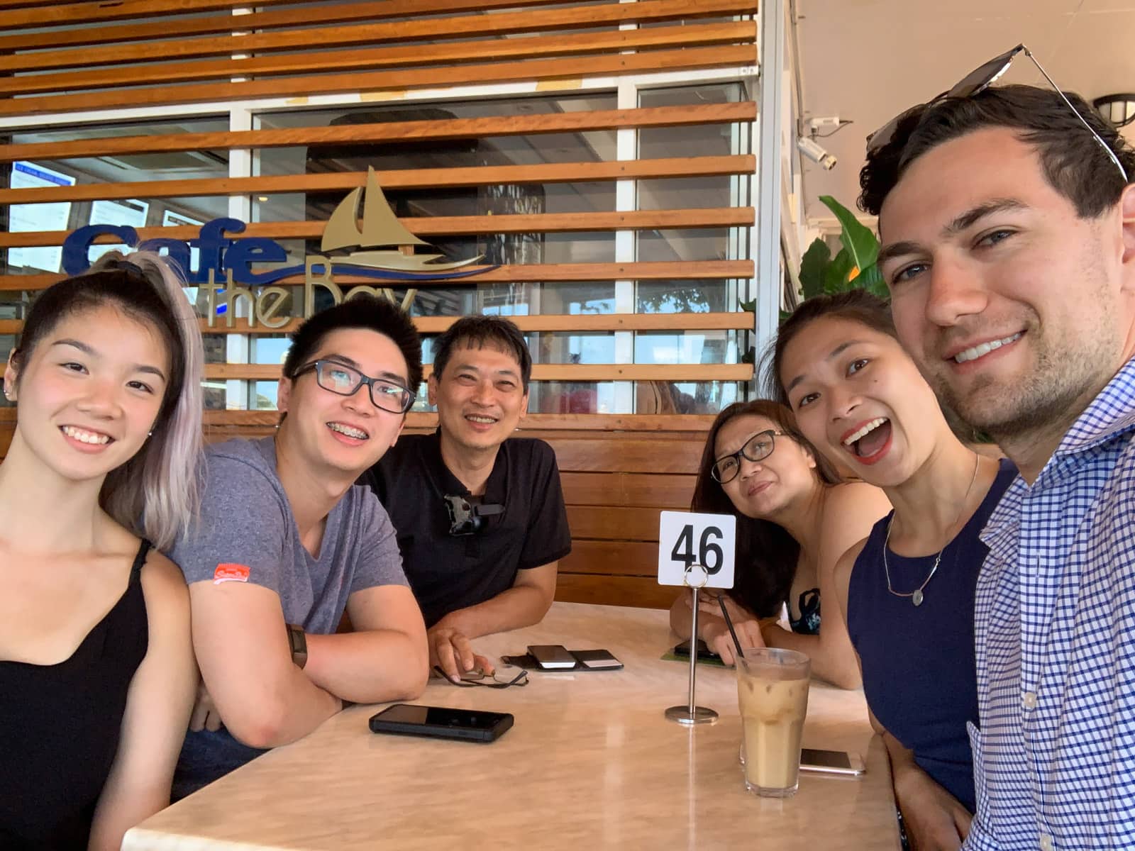 Six people sitting at a wooden lunch table (three people on each side) smiling widely