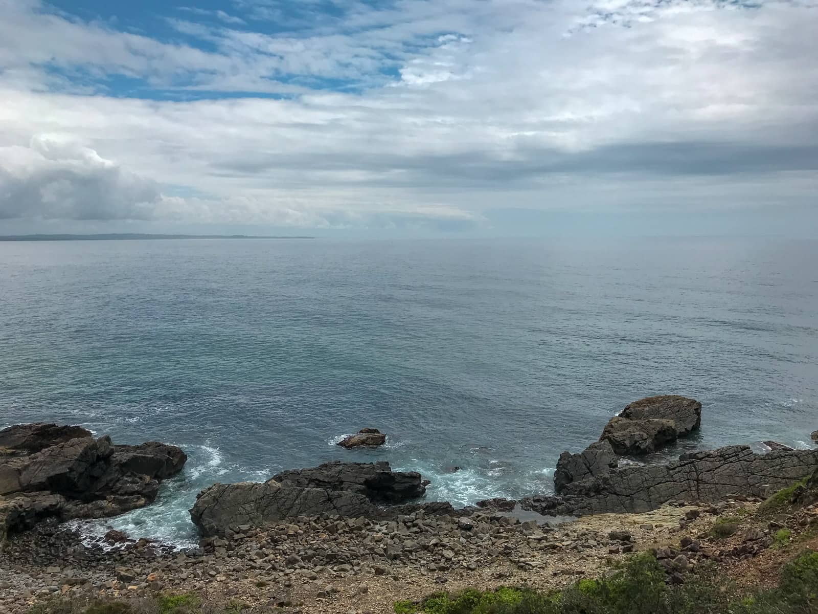 A view of the ocean, with a cloudy sky. In the foreground were some large rocks which are also partially immersed in the water.