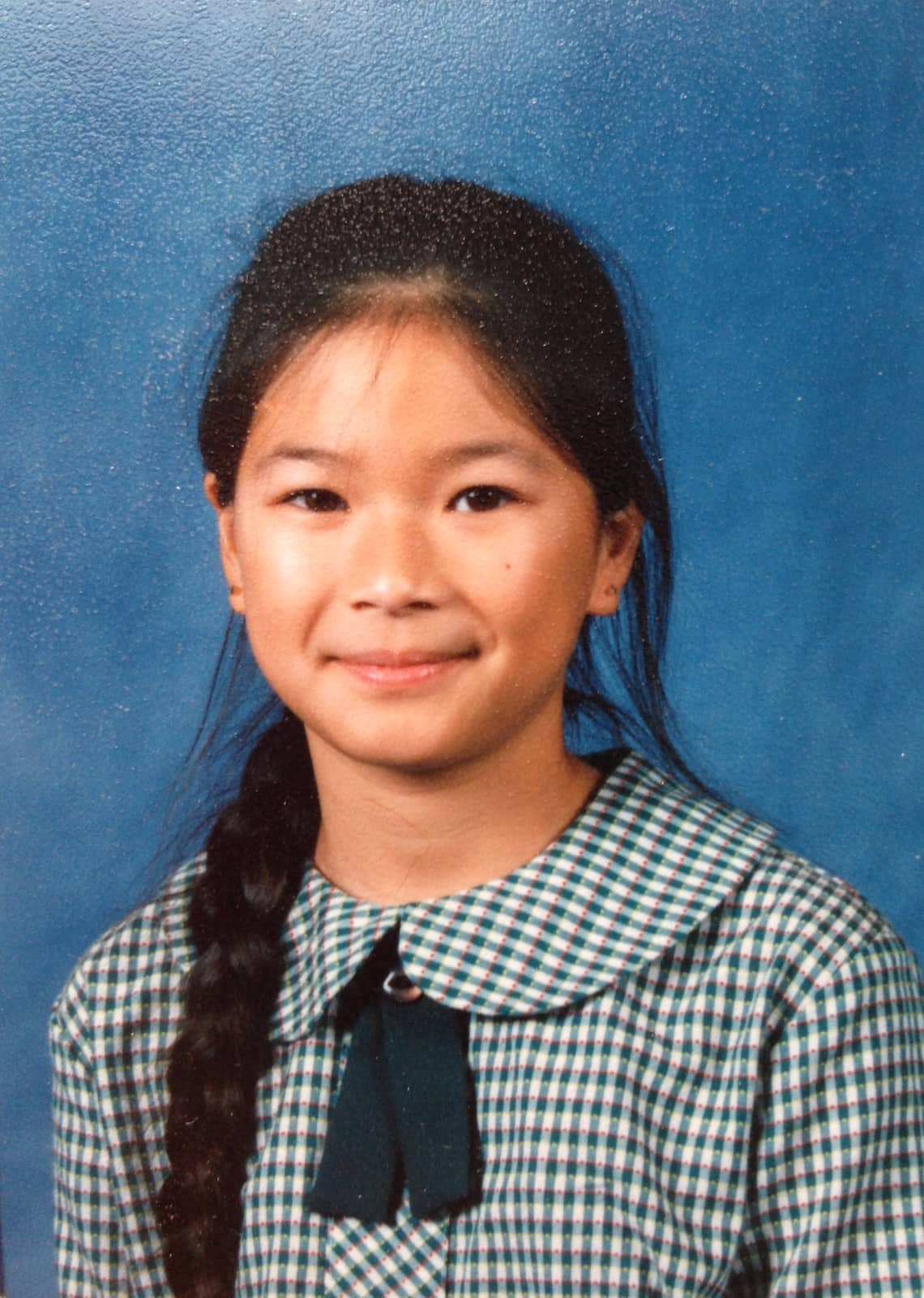 A girl in her school photo, in uniform, with her braided hair placed over her shoulder and in front.