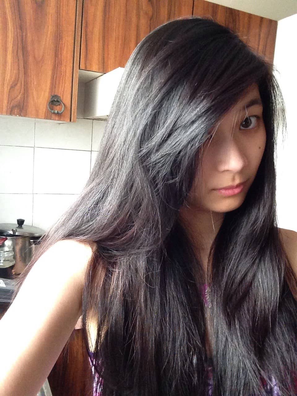 A girl taking a selfie with part of her long hair covering the side of her face. Her hair is black-purple in colour.