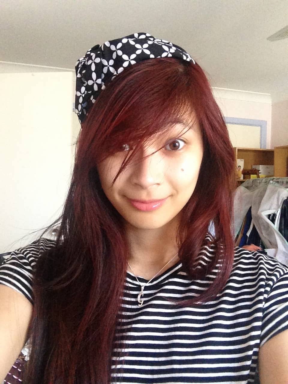 A woman with long red hair, taking a selfie. She has a black and white headband on and is wearing a black and white striped shirt.