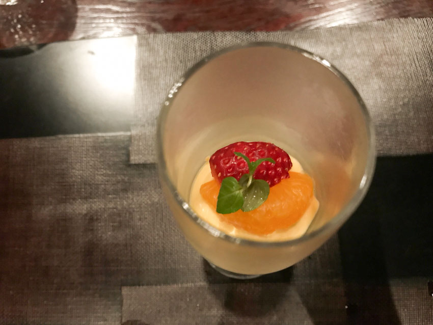 Top-down view of a glass with soft yellow mousse topped with a piece of mandarin orange and piece of strawberry
