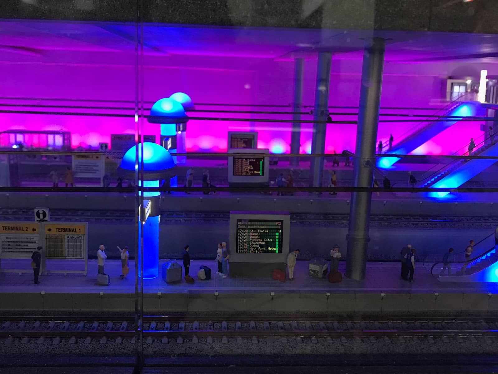 A miniature underground subway with miniature figurines waiting with baggage, and a LED board showing departure and arrival times