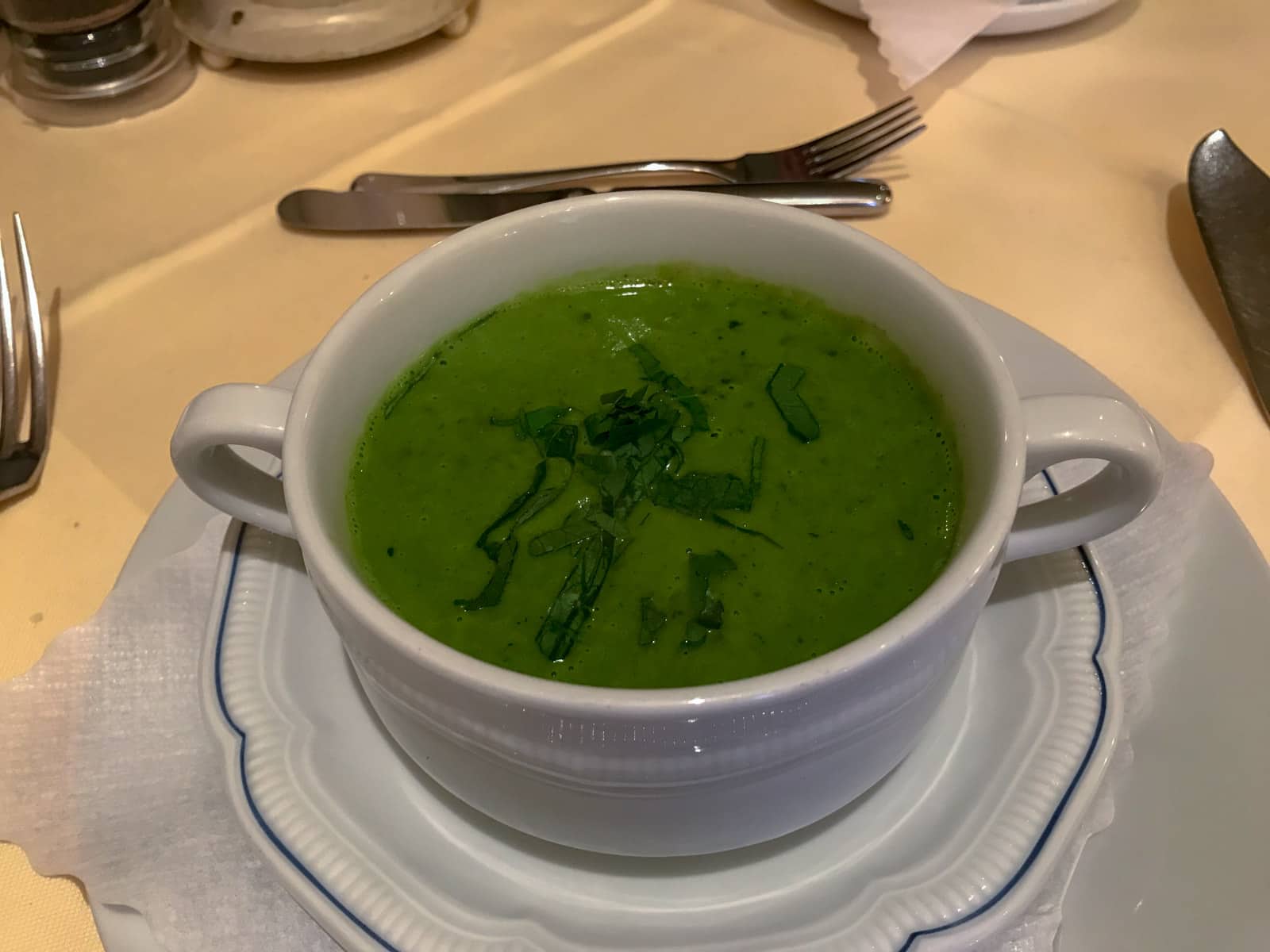 A small white crockery pot with two handles on either side, with green soup in it.