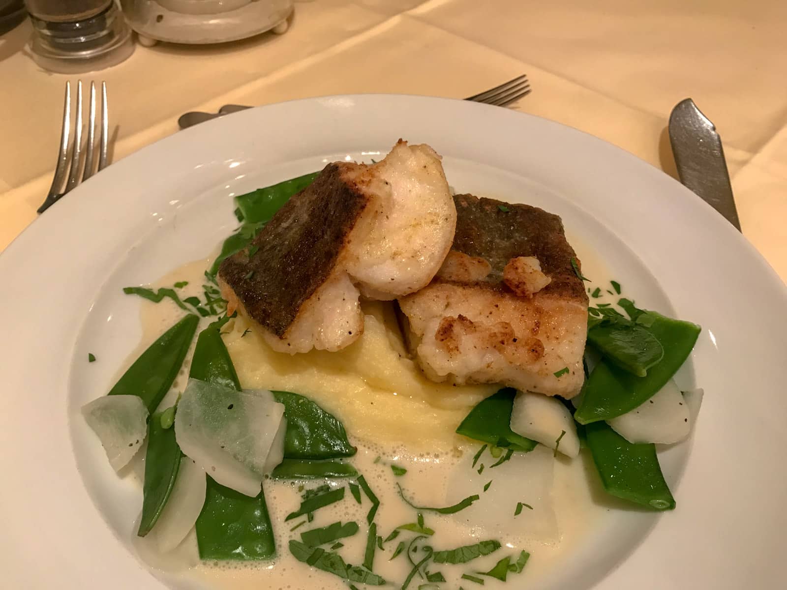 A round white plate with mashed potato, snow peas and fish served on it.