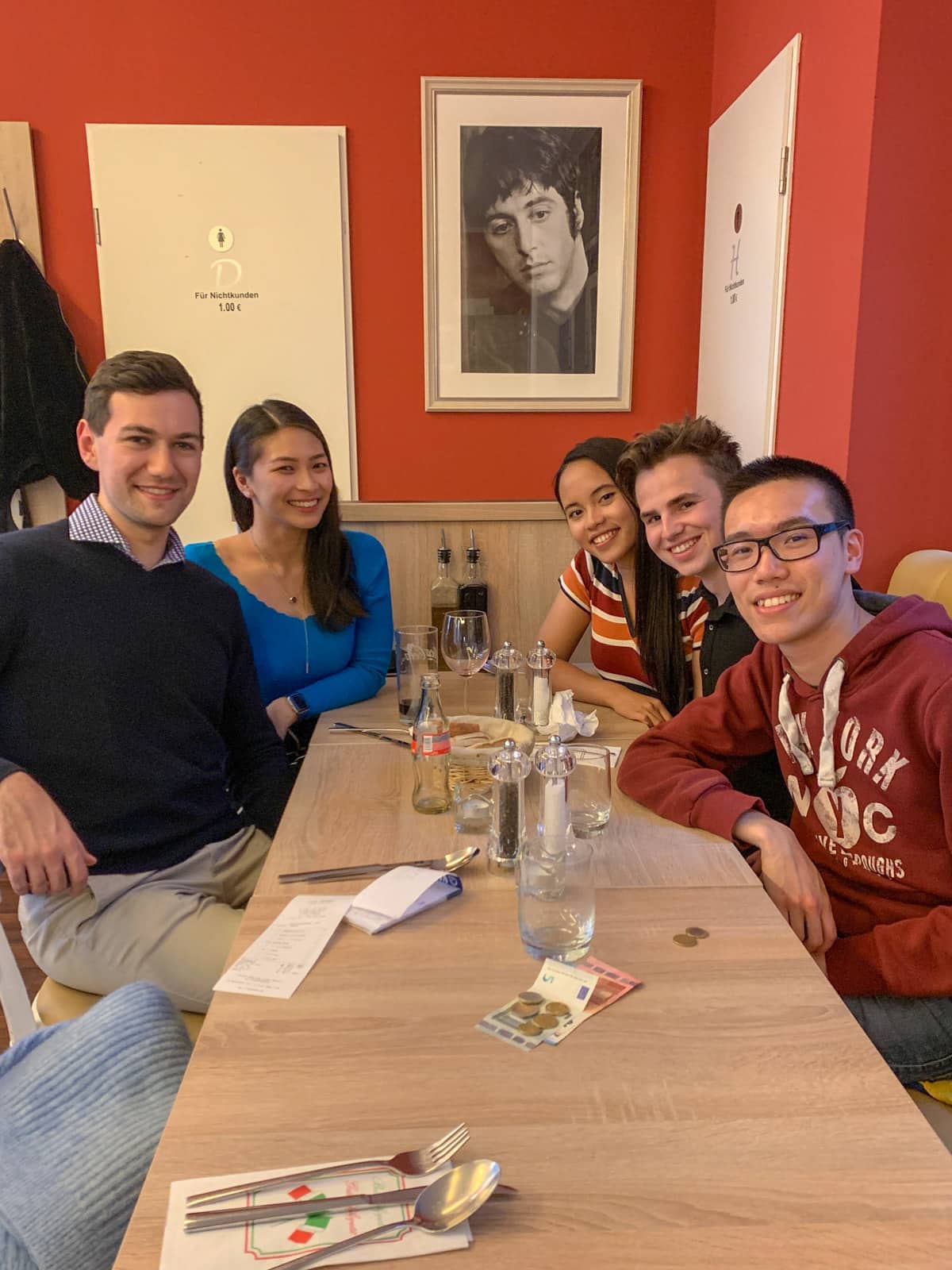 Five people sitting around a long table in a restaurant, two on one side and three on the other. There are some glasses and cups on the table. Everyone is smiling