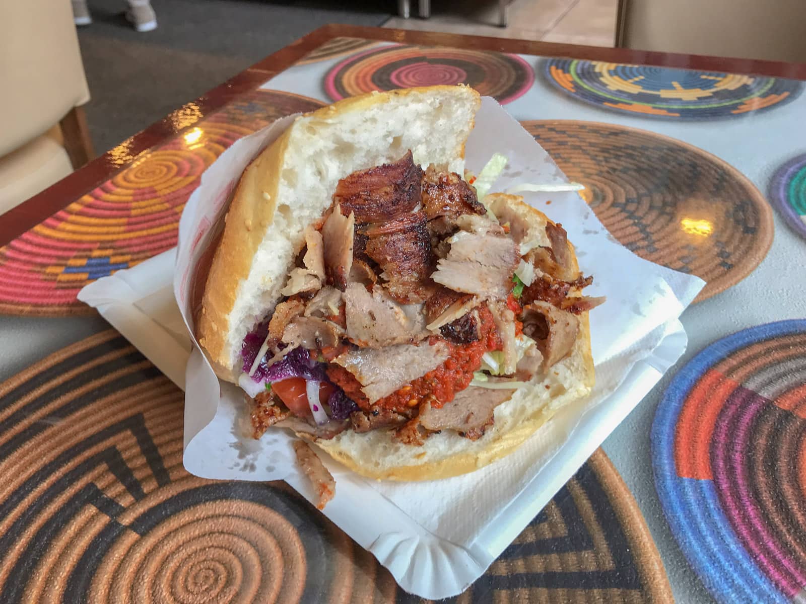 A kebab sandwich filled with pieces of beef and cabbage, on a table with a colourful print