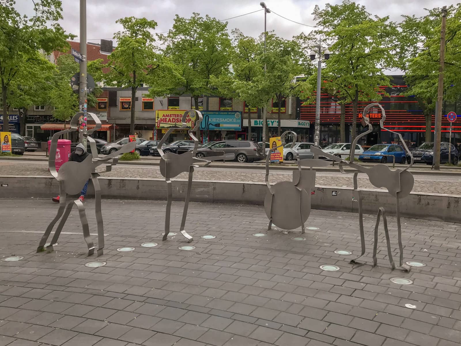 Four outlined metal statue figurines in an open area of tiled concrete
