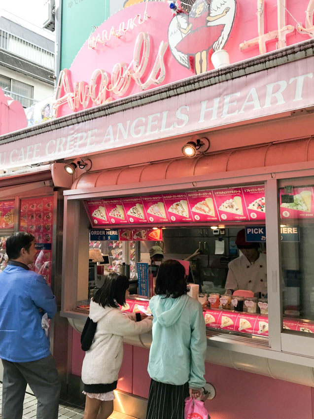 Two girls and a man waiting in front of a kiosk serving food. Menu items are visible on a panel above the kiosk window