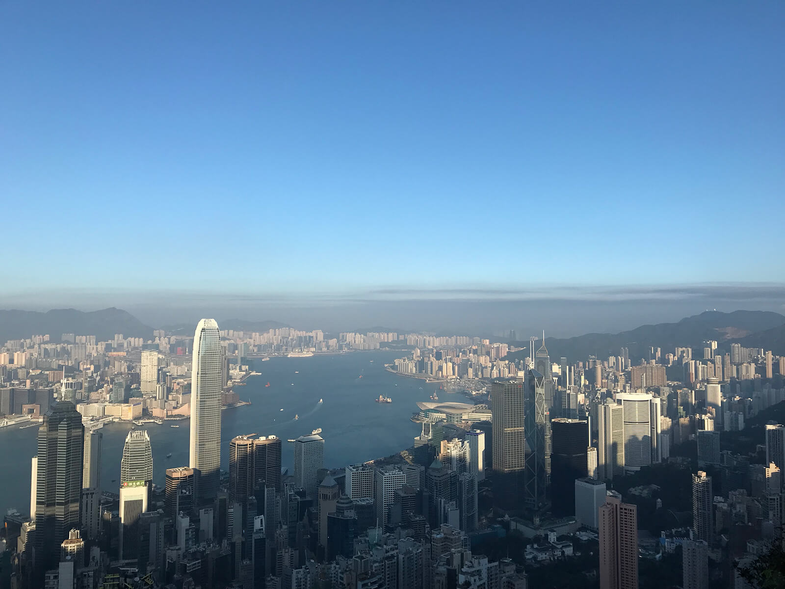 The city of Hong Kong seen from a high altitude, consisting mostly of skyscrapers and ocean in the background. It’s a late afternoon photo