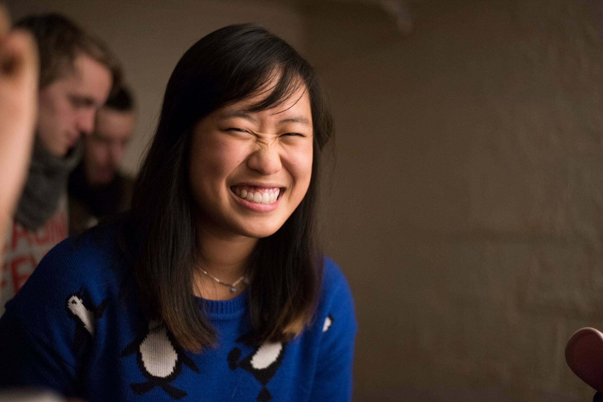 A woman with short dark hair, grinning. She is wearing a blue sweater with penguins