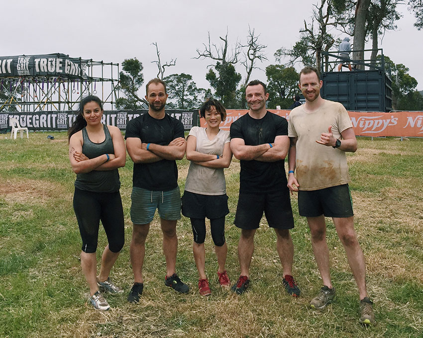 Five people, two women and three men, looking accomplished. Four have their arms folded while one man has a hand in a “hang loose” sign (thumb and last finger extended).