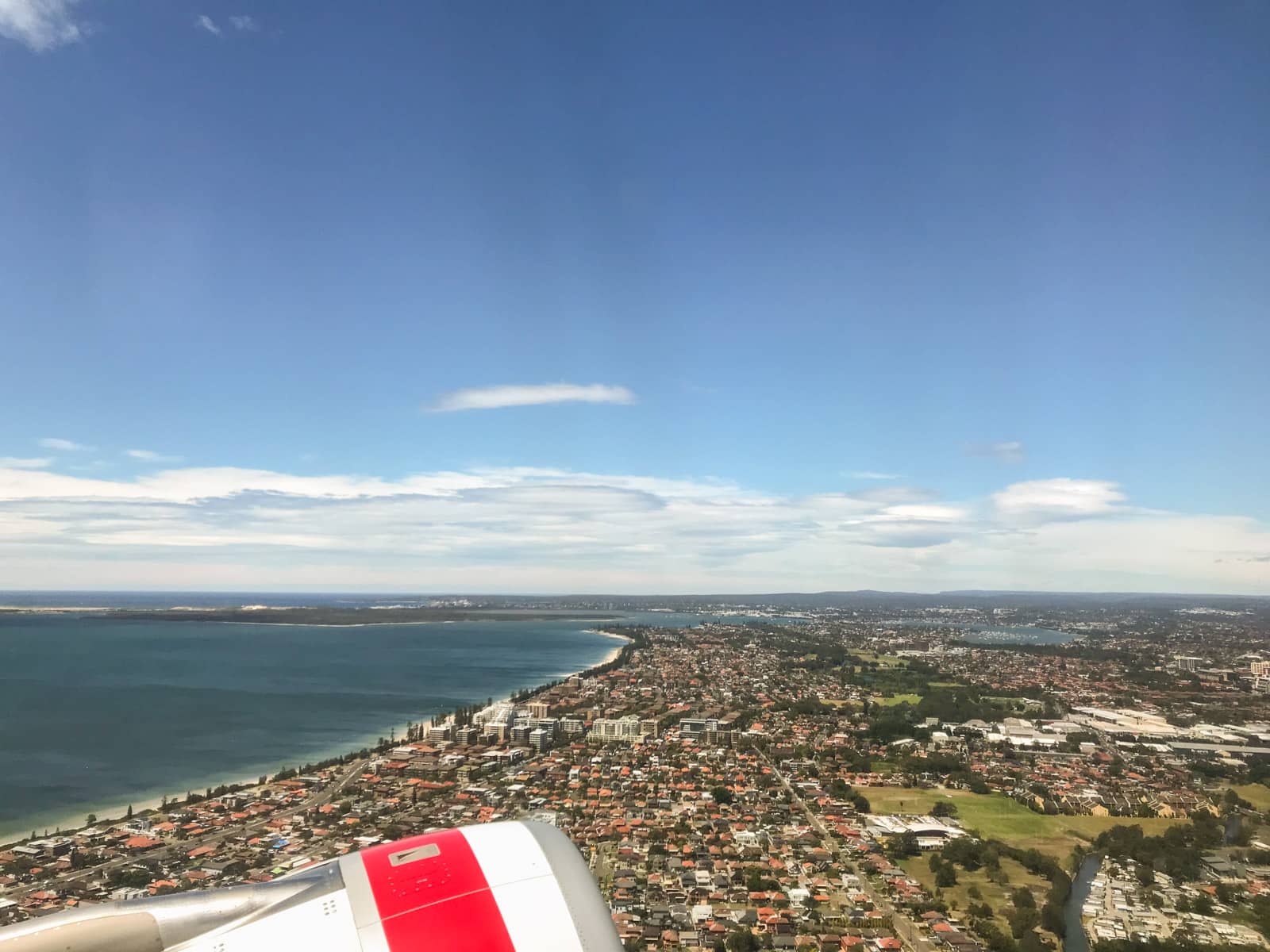 The view from the side of a plane, of the city of Sydney. It is during the day and the sky is blue