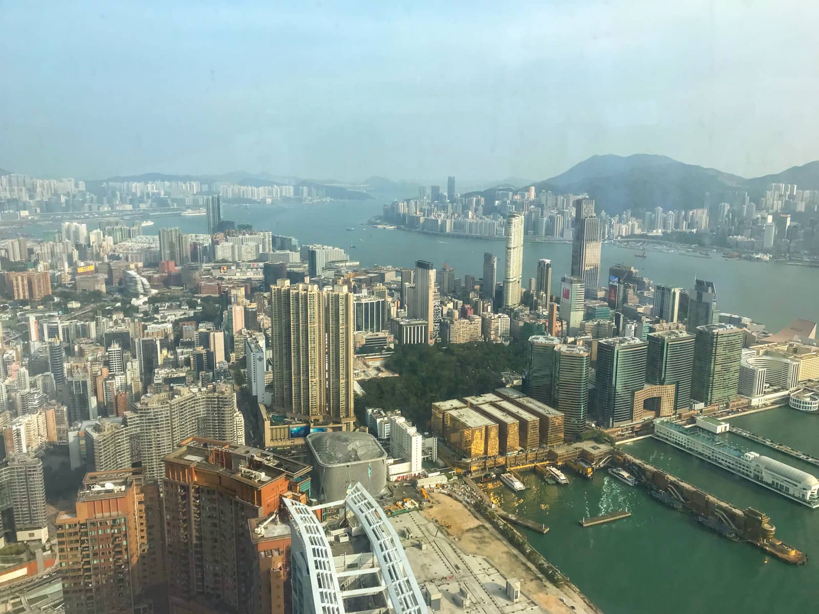 A view of the city of Hong Kong, with the harbour and many buildings visible, seen from the inside of a glass window at a high vantage point