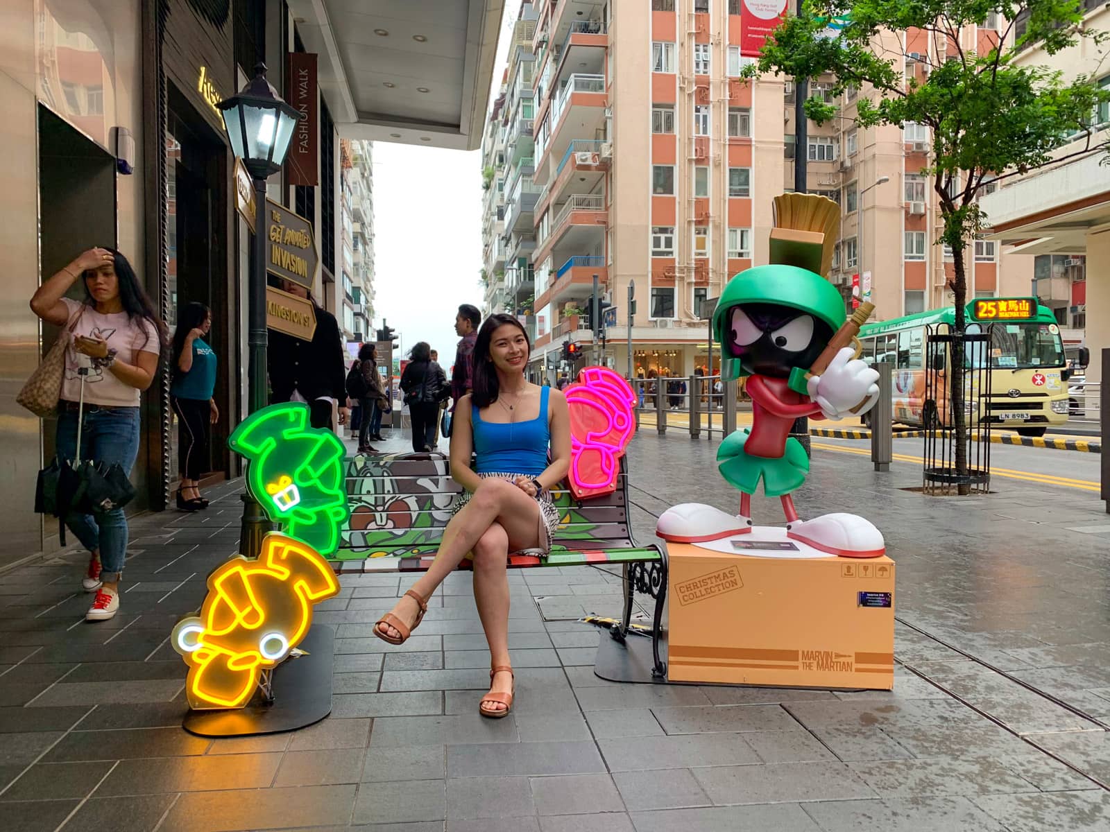 A woman sitting on a Looney Tunes stylised bench. A life size statue of the Marvin the Martian character is sitting next to the bench