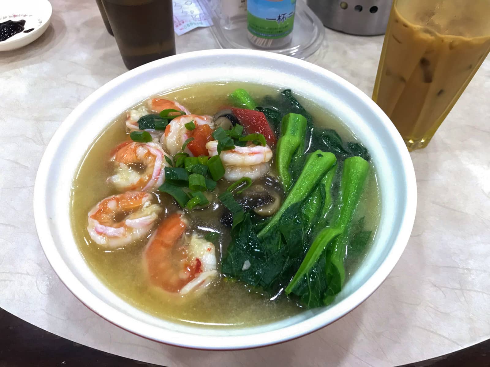 A bowl of soup with Asian greens, many prawns and some other vegetables