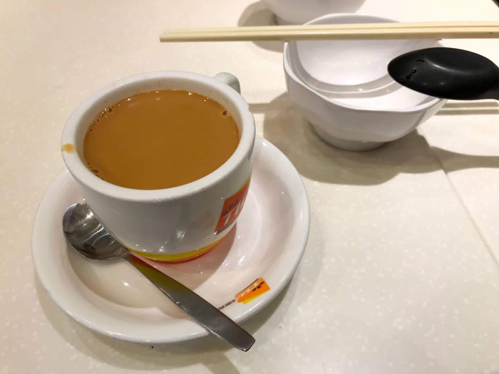 A small white cup of Hong Kong style milk tea, served on a small saucer