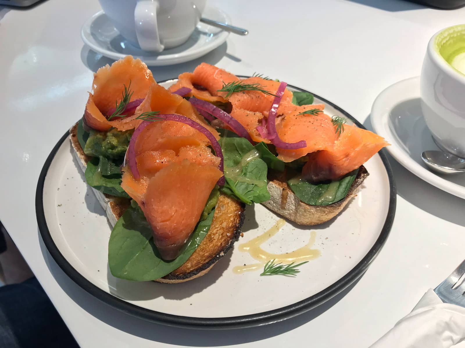 Smoked salmon with spinach served with onion on toasted bread, presented on a round white dish.