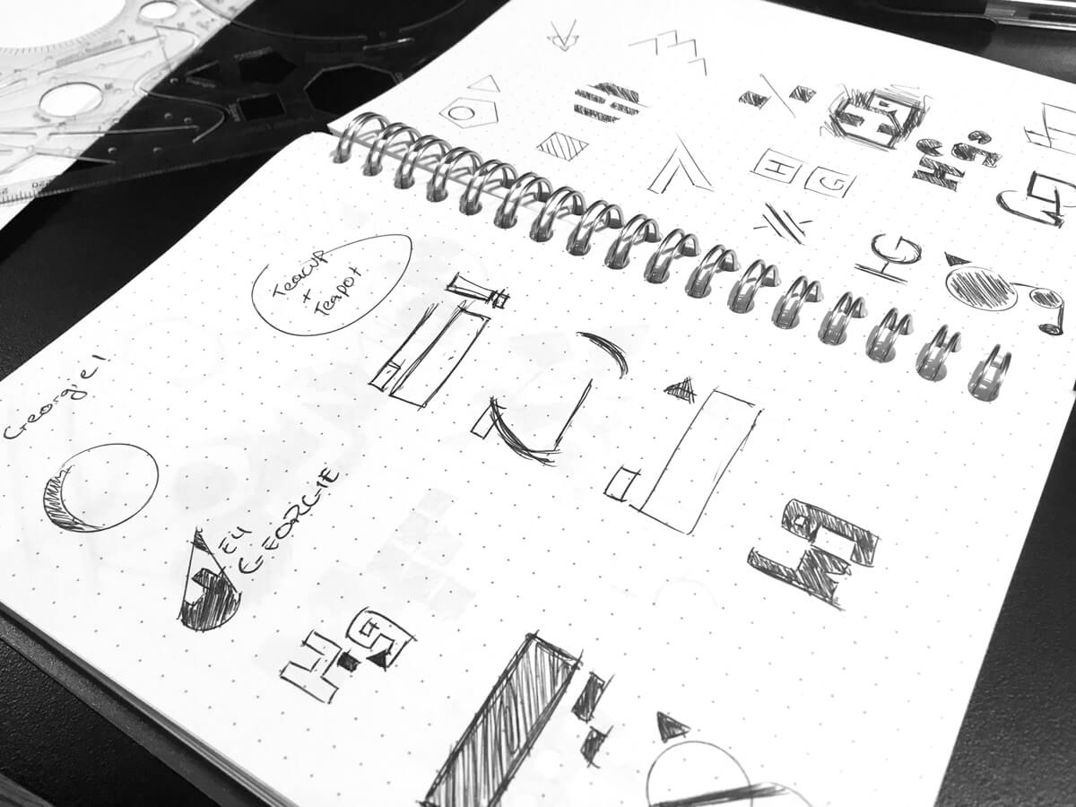 A dot grid spiral bound notebook with various logo sketches