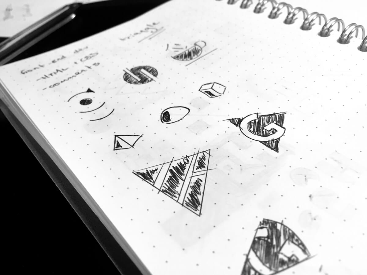 A dot grid spiral bound notebook with various logo sketches, most of which are triangles