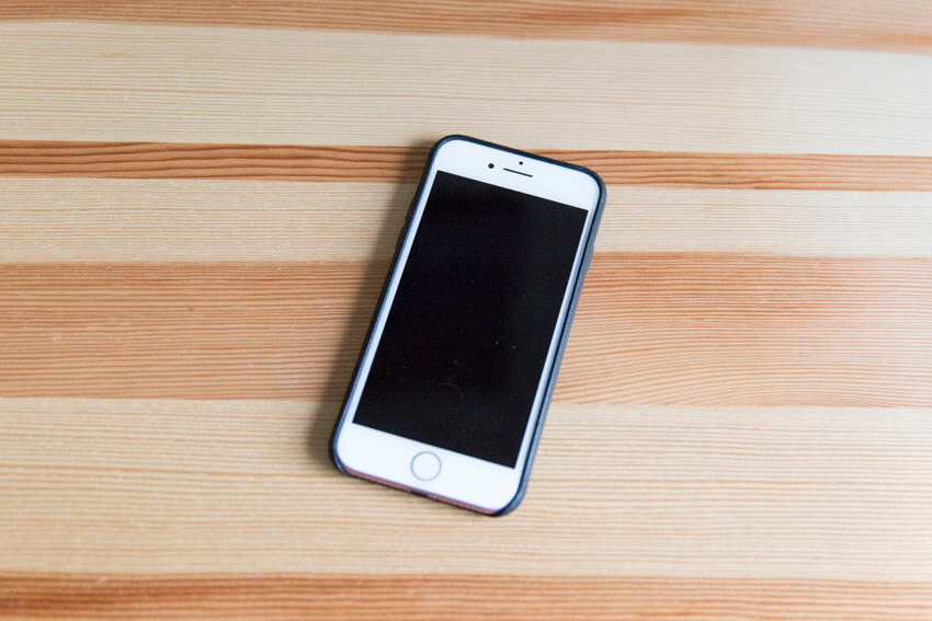 An iPhone with a black leather case, screen-up on a wooden surface