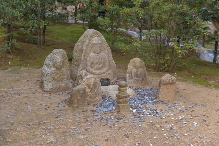 A small set of statues with a silver bowl and a lot of coins surrounding it