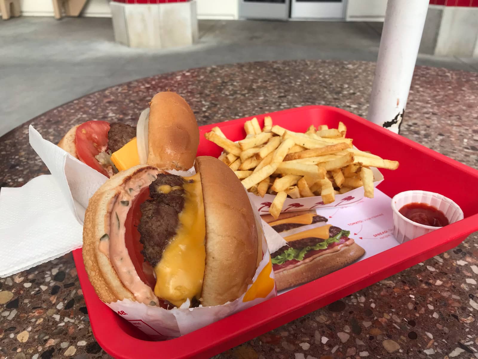 A red basket tray with a couple of burgers and a handful of fries, with a small tub of tomato sauce